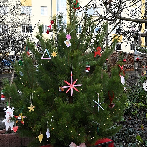 Ein Weihnachtsbaum mit vielen selbstgebastelten Anhängern steht im Garten des Kindergartens.