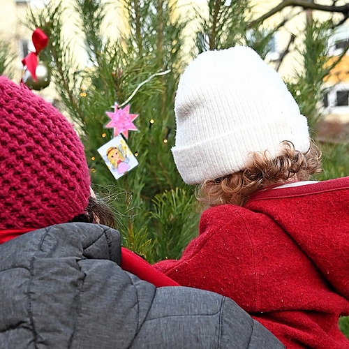 Ein Kind und ein Elternteil hängen zusammen eine selbstgebastelte Figur an den Weihnachtsbaum.