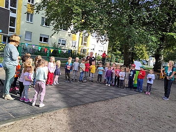 Foto von Kindern und Erwachsenen, die im Garten des Kindergartens im Kreis stehen und gemeinsam singen