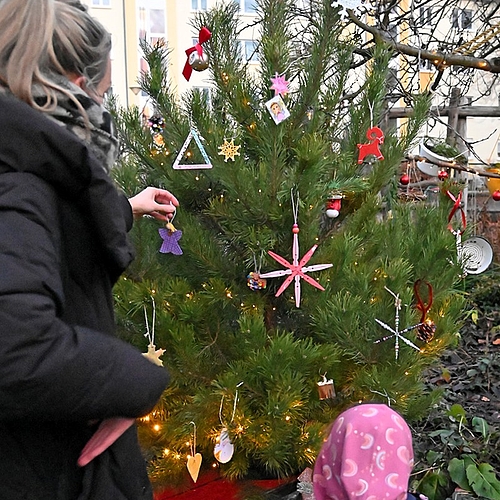 Eine pädagogische Fachkraft und ein Kind hängen gemeinsam Weihnachtsdeko an einen Baum.